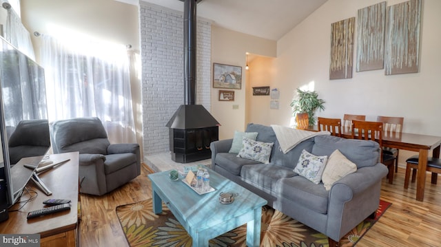 living room with a wood stove, light hardwood / wood-style flooring, and vaulted ceiling