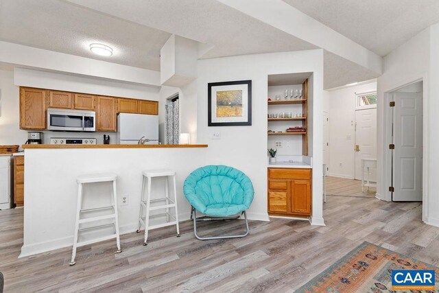 kitchen with light wood-type flooring, white refrigerator, a kitchen bar, and kitchen peninsula