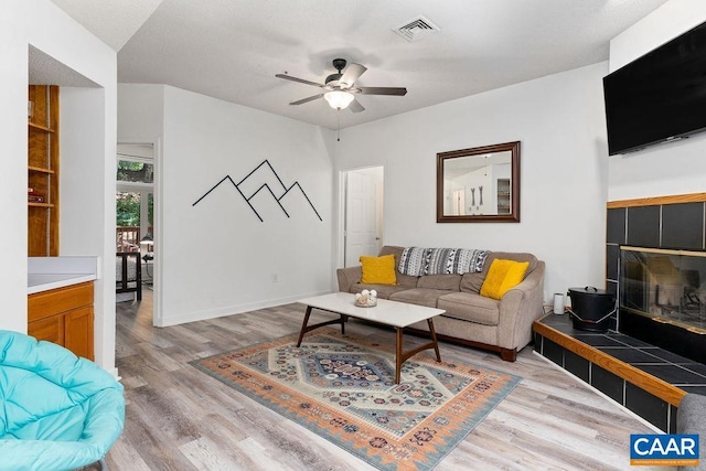 living room featuring light wood-type flooring, a tiled fireplace, and ceiling fan