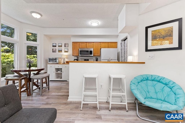 kitchen featuring a textured ceiling, a kitchen bar, kitchen peninsula, white refrigerator, and light wood-type flooring