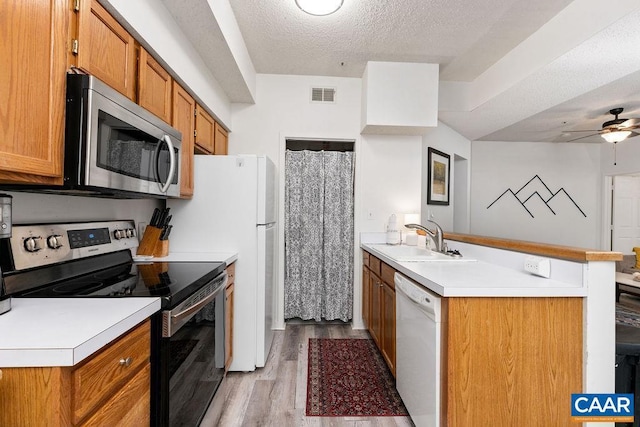 kitchen featuring a textured ceiling, stainless steel appliances, sink, ceiling fan, and light hardwood / wood-style floors