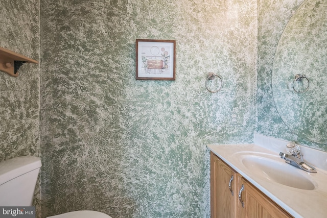 bathroom featuring vanity, toilet, and wallpapered walls