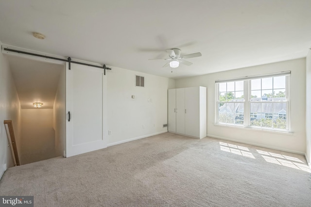 unfurnished bedroom with a barn door, visible vents, a ceiling fan, and light colored carpet