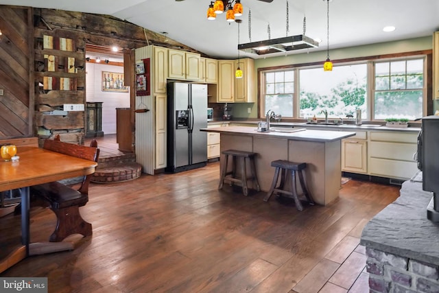 kitchen with lofted ceiling, stainless steel refrigerator with ice dispenser, dark wood-type flooring, a breakfast bar area, and a center island with sink