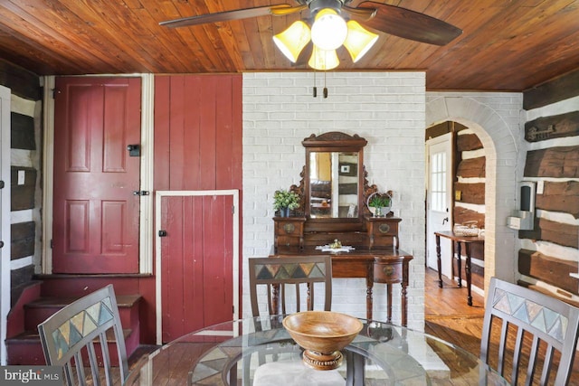 dining area featuring brick wall, wood walls, wooden ceiling, hardwood / wood-style flooring, and ceiling fan