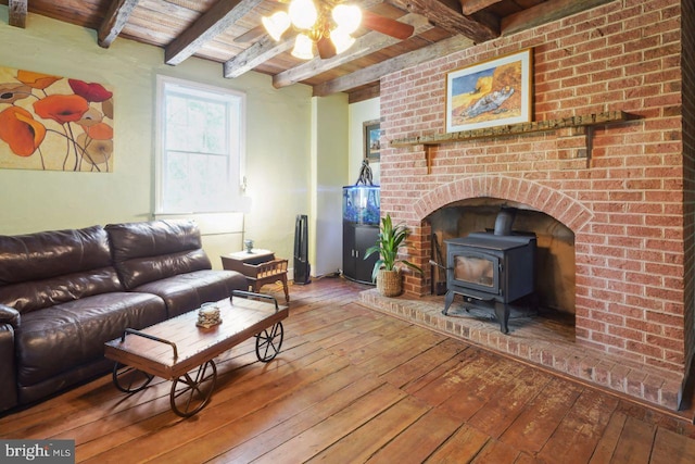 living room featuring a wood stove, ceiling fan, beamed ceiling, and hardwood / wood-style flooring