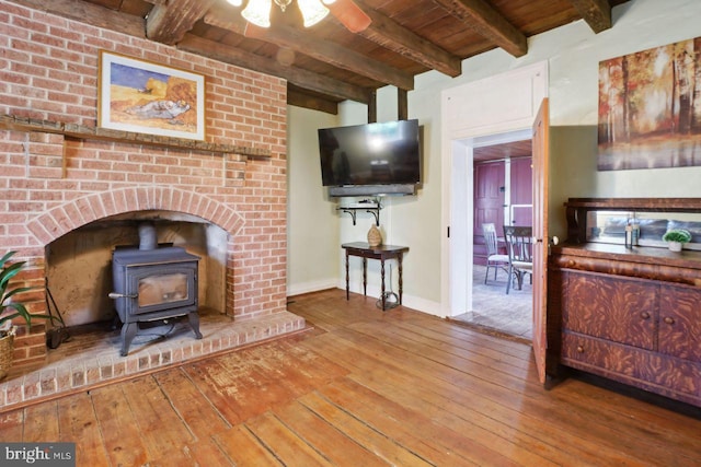 living room with hardwood / wood-style flooring, ceiling fan, a wood stove, and beam ceiling