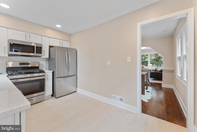 kitchen with light stone countertops, stainless steel appliances, white cabinets, and light hardwood / wood-style floors