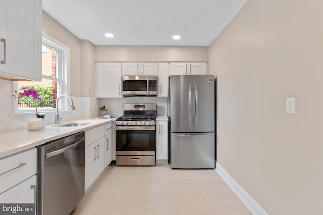 kitchen with tasteful backsplash, sink, appliances with stainless steel finishes, white cabinets, and light hardwood / wood-style floors