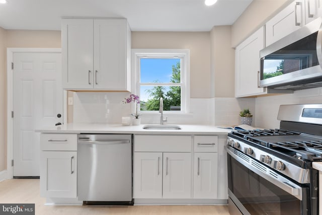 kitchen with light hardwood / wood-style flooring, backsplash, appliances with stainless steel finishes, sink, and white cabinets