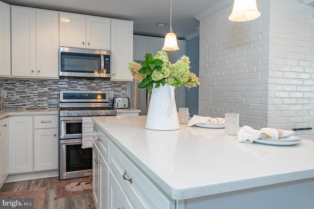 kitchen featuring crown molding, appliances with stainless steel finishes, white cabinetry, wood-type flooring, and pendant lighting