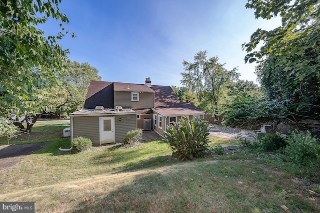 rear view of property featuring an outdoor structure, a lawn, and central AC