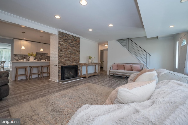 living room featuring ornamental molding, a stone fireplace, and wood-type flooring