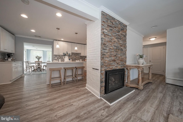 living room with a large fireplace, ornamental molding, and light hardwood / wood-style floors