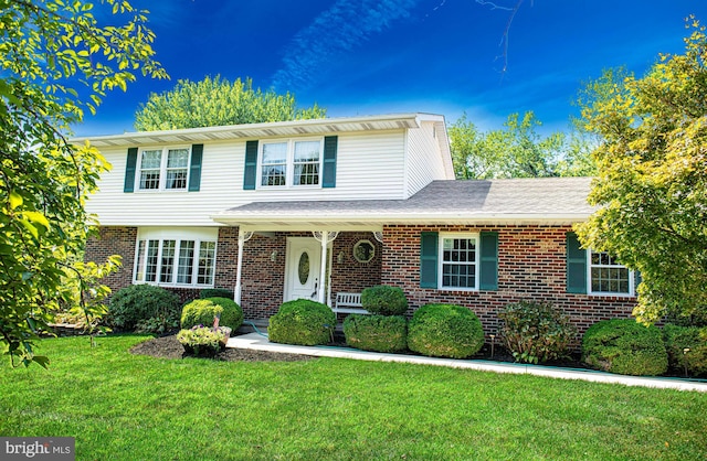 traditional home featuring covered porch, brick siding, and a front yard