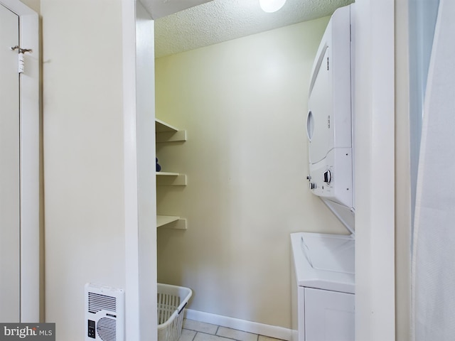 clothes washing area featuring stacked washer / dryer, a textured ceiling, and light tile patterned flooring