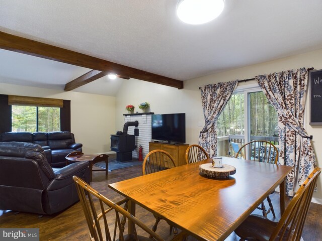 dining room with a healthy amount of sunlight, vaulted ceiling with beams, a wood stove, and dark hardwood / wood-style flooring