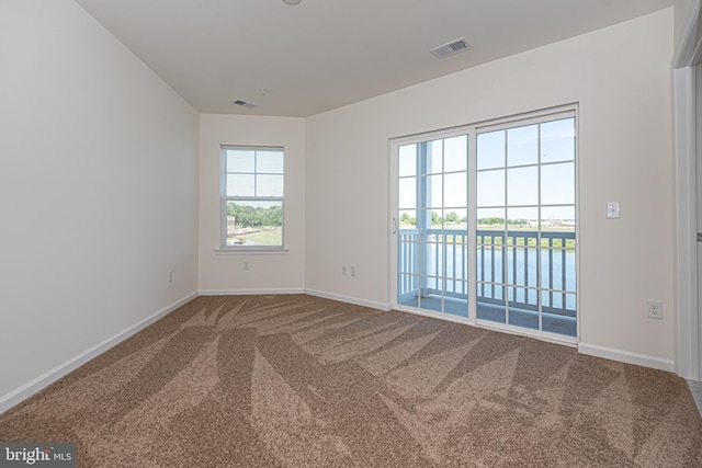 carpeted empty room with a water view, baseboards, and visible vents