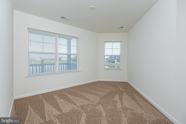 spare room featuring carpet, visible vents, and baseboards