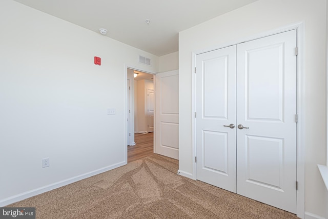 unfurnished bedroom featuring a closet, visible vents, light carpet, and baseboards