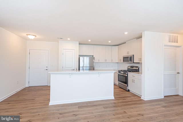 kitchen with appliances with stainless steel finishes, a breakfast bar area, light countertops, and light wood finished floors