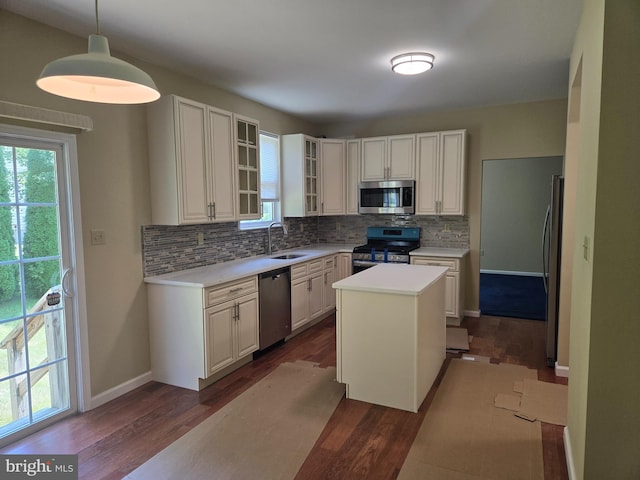 kitchen with hanging light fixtures, stainless steel appliances, dark wood-type flooring, a kitchen island, and decorative backsplash