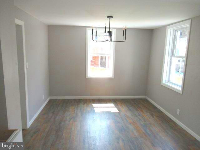 unfurnished dining area featuring dark hardwood / wood-style flooring, a healthy amount of sunlight, and an inviting chandelier