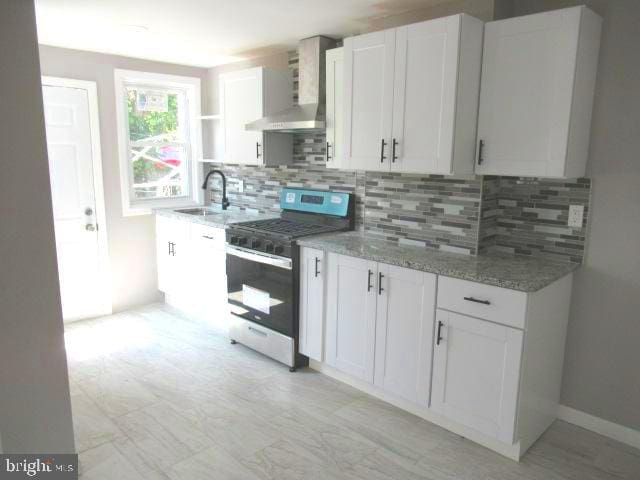 kitchen featuring gas stove, white cabinetry, sink, wall chimney range hood, and decorative backsplash