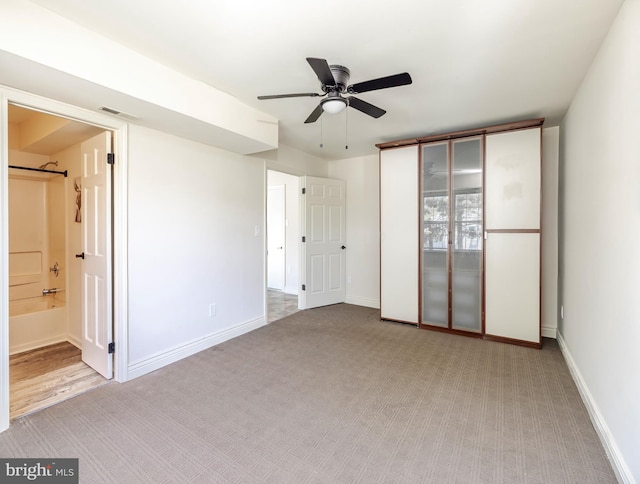 unfurnished bedroom featuring light colored carpet, ensuite bath, and ceiling fan