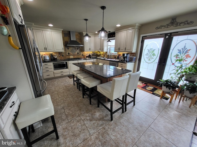 kitchen with a breakfast bar area, appliances with stainless steel finishes, french doors, backsplash, and wall chimney exhaust hood