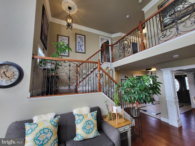 interior space featuring wood finished floors, a towering ceiling, stairs, ornamental molding, and ornate columns