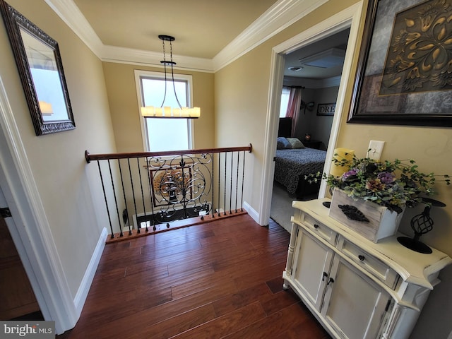 hallway featuring a chandelier, dark wood-type flooring, an upstairs landing, baseboards, and ornamental molding