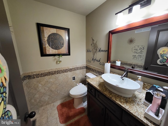 half bathroom with toilet, vanity, visible vents, tile walls, and wainscoting