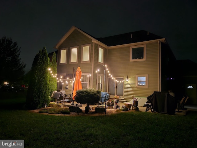 back of house at night with a yard and a patio