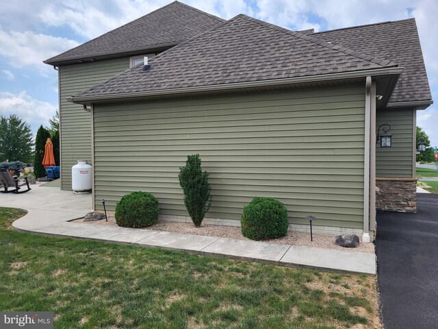 view of side of property featuring a yard, roof with shingles, and a patio area