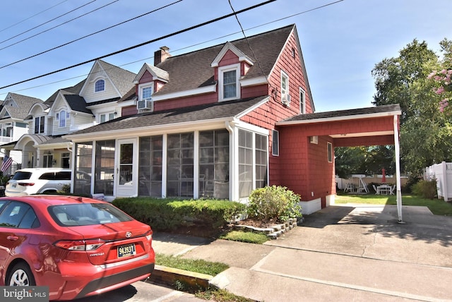 view of front facade with a shingled roof, a residential view, concrete driveway, a chimney, and a sunroom