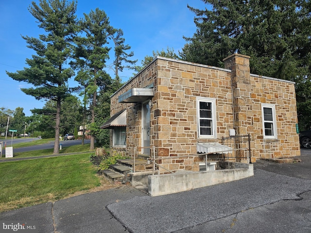 exterior space featuring stone siding, a lawn, and a chimney