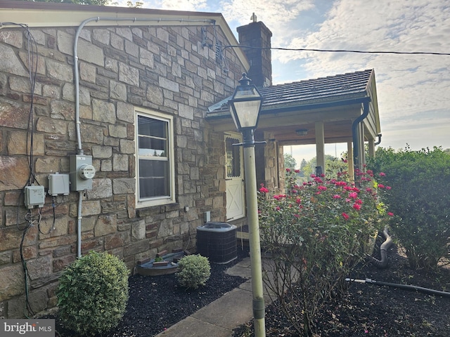 view of side of home featuring central AC, a chimney, and stone siding