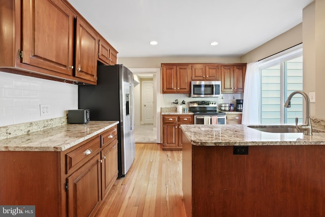 kitchen featuring light stone counters, stainless steel appliances, sink, light hardwood / wood-style floors, and kitchen peninsula