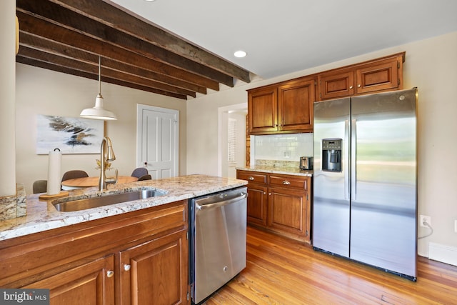 kitchen with light wood-type flooring, pendant lighting, sink, backsplash, and appliances with stainless steel finishes