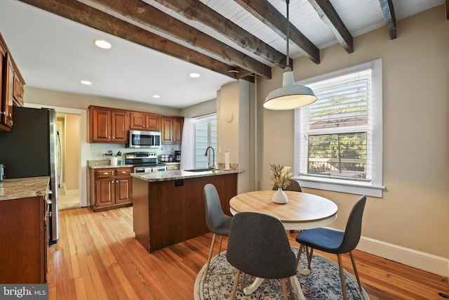 kitchen with light wood-type flooring, light stone countertops, sink, hanging light fixtures, and appliances with stainless steel finishes