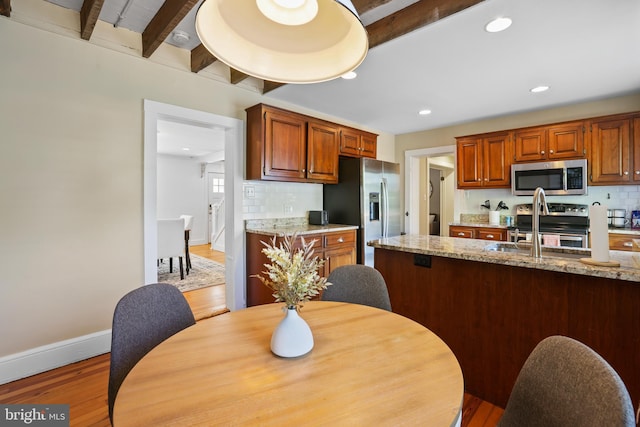 kitchen featuring light wood-type flooring, beam ceiling, decorative backsplash, light stone countertops, and appliances with stainless steel finishes