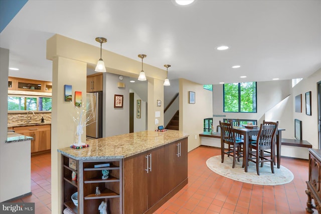 kitchen featuring hanging light fixtures, light stone countertops, sink, stainless steel fridge, and tasteful backsplash