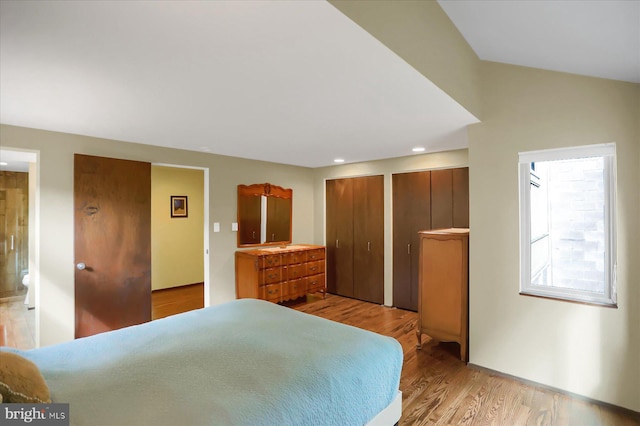 bedroom featuring light hardwood / wood-style flooring, ensuite bath, vaulted ceiling, and multiple closets