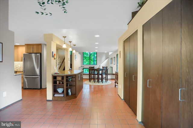 kitchen featuring tile patterned floors, stainless steel fridge, tasteful backsplash, decorative light fixtures, and light stone counters