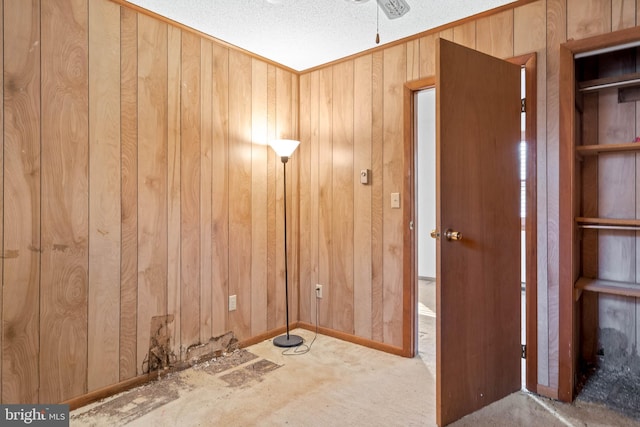 carpeted empty room with wooden walls, ceiling fan, and a textured ceiling