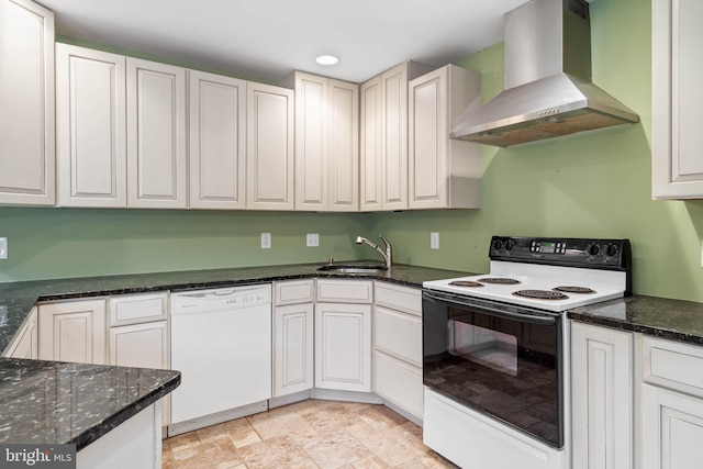 kitchen with white cabinetry, sink, wall chimney exhaust hood, dark stone countertops, and white appliances