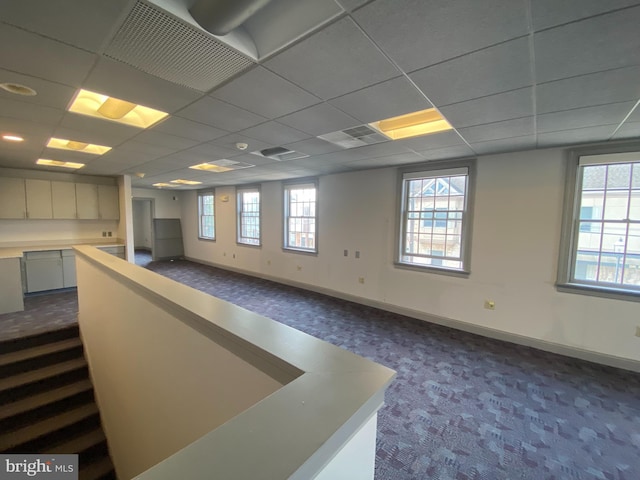 empty room featuring dark colored carpet, a paneled ceiling, plenty of natural light, and baseboards