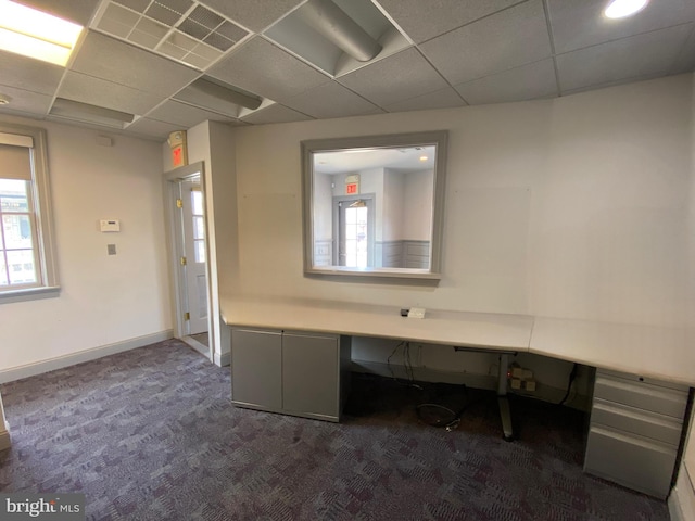 unfurnished office with visible vents, baseboards, a paneled ceiling, built in desk, and dark colored carpet