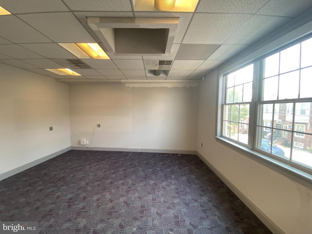 empty room with dark colored carpet and a drop ceiling